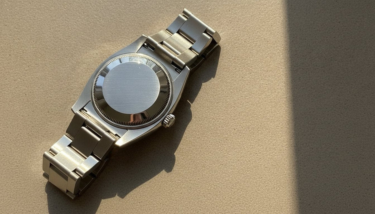 The caseback and Oyster bracelet of a pre-owned steel Rolex, set face-down on grey stone