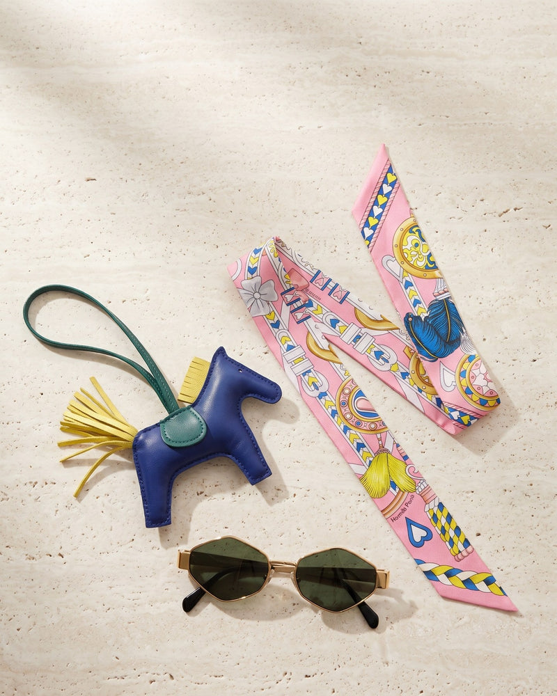 A Hermès Rodeo bag charm, a pink Hermès Twilly and Celine sunglasses on travertine