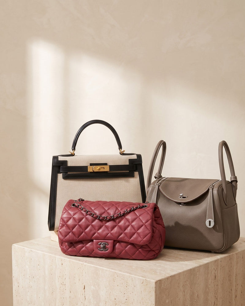 A Hermès Kelly 28 in canvas, a Hermès Lindy 30 in étoupe and a red quilted Chanel flap bag on a travertine plinth