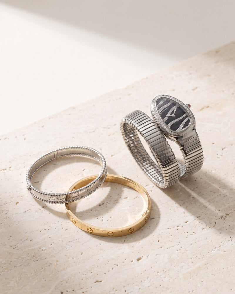 A Cartier Love bracelet, a Van Cleef & Arpels Perlée bangle and a Bvlgari Serpenti Tubogas watch on travertine